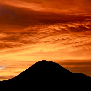 Dark silhouette of Mt Ngauruhoe with a bright red and orange sky at sunrise 