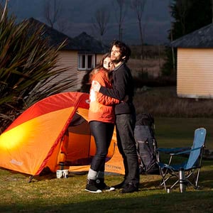 Tent and couple hugging one another at Discovery Lodge with camping huts in the background