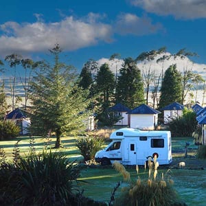 A Mighty Camper van in a powered site at Discovery Lodge with Camping huts in background