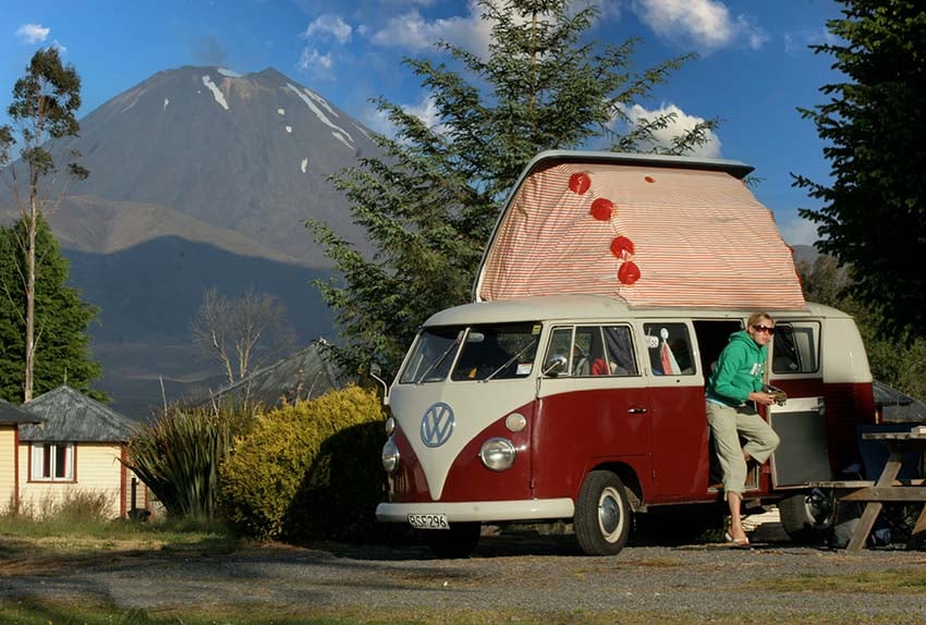 A Volkswagen camper van and a female at a powered camper site at Discovery Lodge Tongariro with Mt Ngauruhoe in view