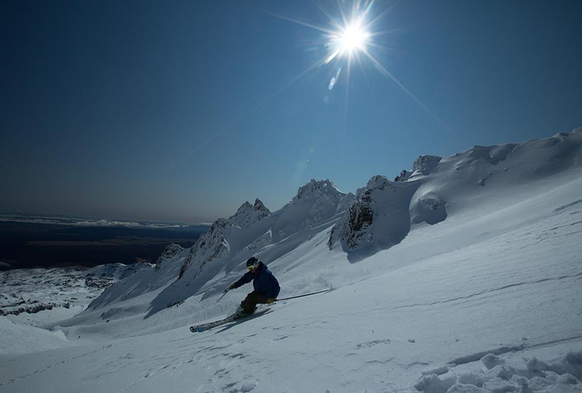A skier skiing with the Pinnacles of Whakapapa Mt Ruapehu in the background
