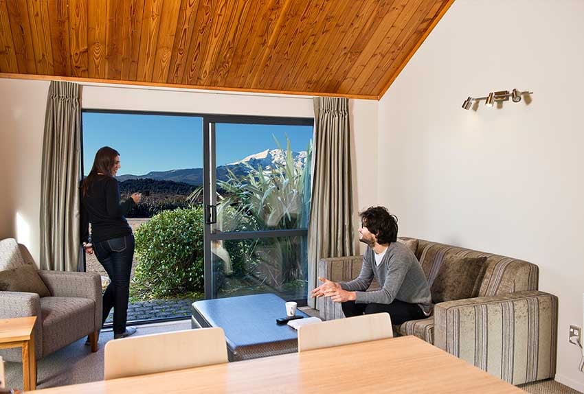 Two people talking in the lounge of a chalet one bedroom at Discovery Lodge Tongariro admiring the view of Mt Ruapehu