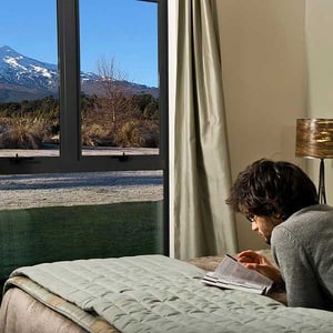 A guest lying on a queen bed reading with views of Mt Ruapehu from a chalet one bedroom unit at Discovery Lodge Tongariro