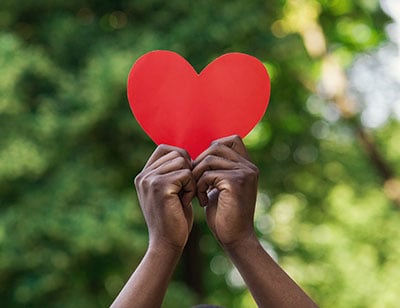 Two hands holding up paper cut out of heart