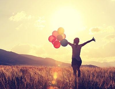 A women running through long grass holding balloons