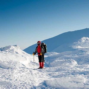 Lone mountaineer dressed in warm clothing standing on snow with blue sky