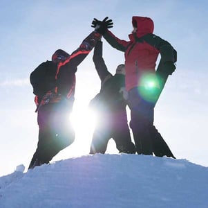 Three people doing high fives at the top of a snowy peak