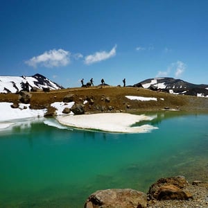 The Emerald Lakes with a little snow and hikers walking the Tongariro Alpine Crossing