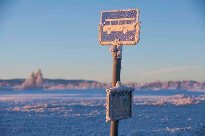 A bus stop sign with frosty ice on it with snow in the background