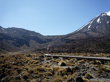 A hiker standing on board walk in the Mangatepopo Valley taking a photo of Mt Ngauruhoe